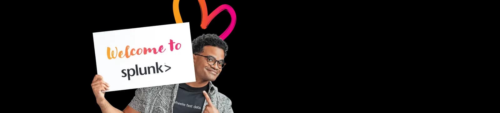Smiling employee holding a large ‘Welcome to Splunk’ sign with colorful heart-shaped graphics on a white background, creating a friendly onboarding banner.