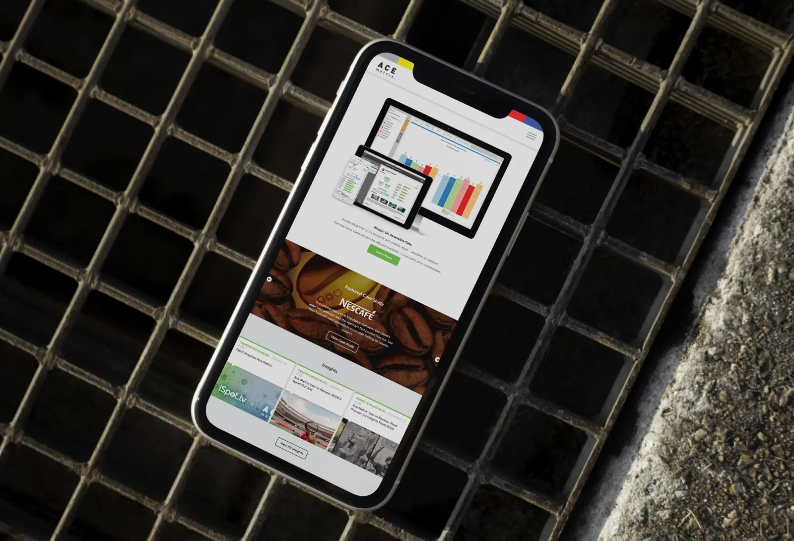 Smartphone lying on metal grate showing ACE Metrix marketing analytics website.